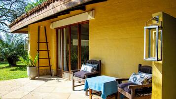 Une terrasse avec deux chaises en bois, une table et une échelle appuyée contre un mur jaune.