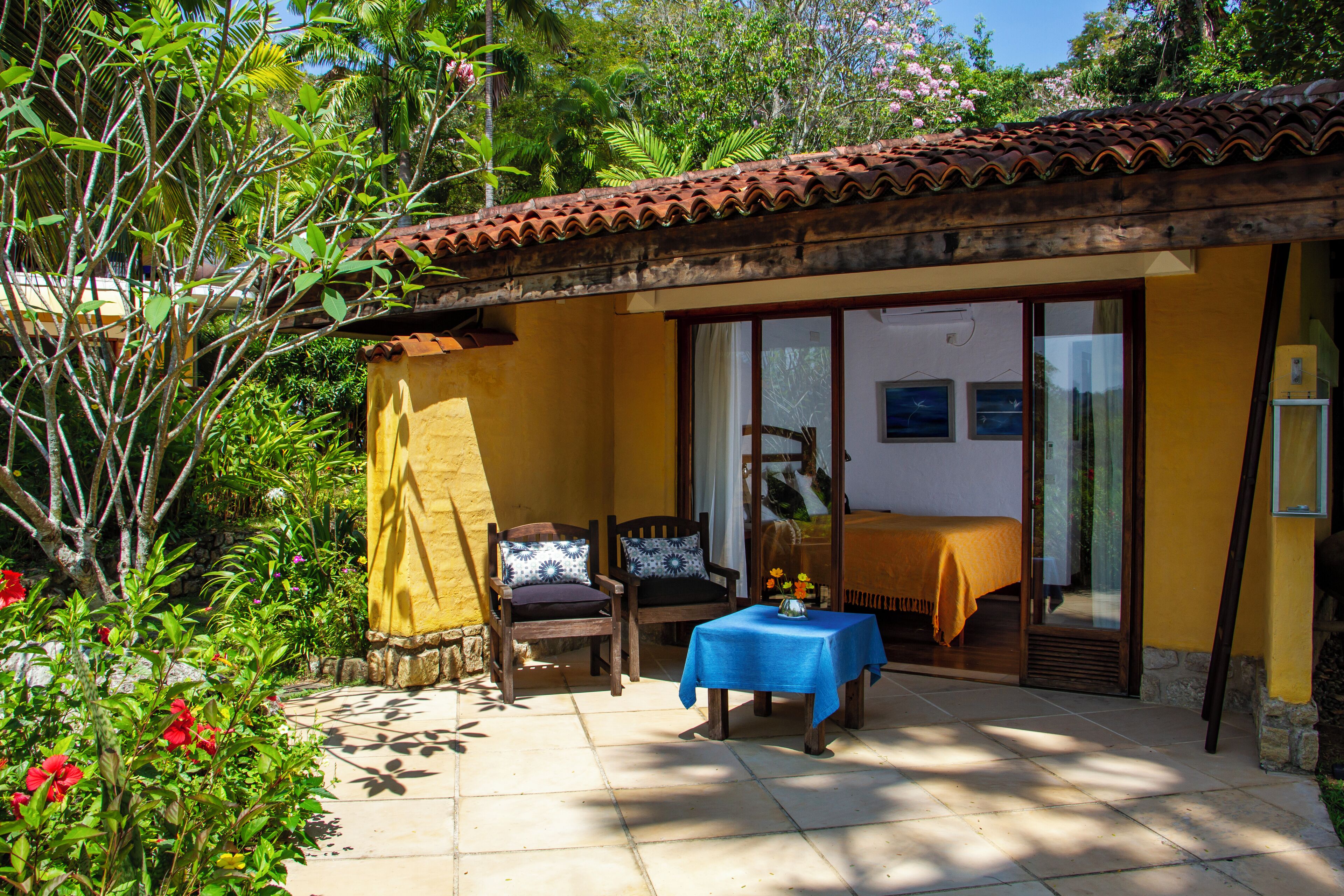 A small, yellow building with a tiled roof, a sliding glass door, and a table with a blue tablecloth.