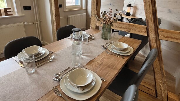 Een eettafel gedekt met borden, kommen, glazen en bestek.