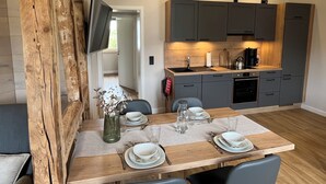 Een moderne keuken met grijze kastjes, een houten eettafel gedekt voor vier personen, en een flatscreen televisie aan de muur bevestigd.
