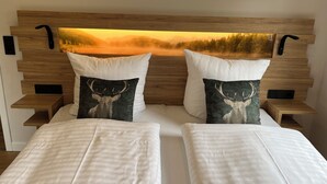 Een tweepersoonsbed met twee kussens, waarvan één met een hertenprint, in een kamer met een houten hoofdeinde en een schilderij van een zonsondergang.