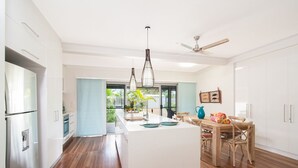 A modern kitchen with a central island, wooden flooring, white cabinetry, and a dining area with a table and chairs.