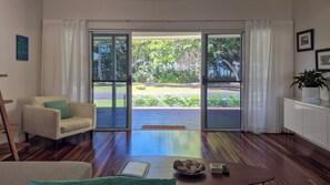 Un salón con sofá, una mesa de centro y vistas a un jardín a través de puertas de cristal.