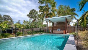 A rectangular swimming pool with clear blue water, surrounded by a wooden fence and lush greenery.