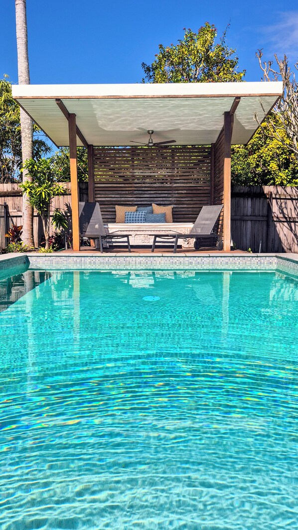 A clear swimming pool with a covered seating area and lounge chairs.