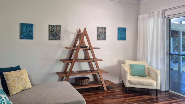 Una habitación con una estantería de escalones de madera, un sofá, una silla y cuatro cuadros decorativos.