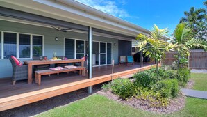 A covered patio with a wooden deck, outdoor seating, and a small garden area with plants and a palm tree.