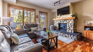 A cozy living room with a stone fireplace, leather sofas, and a flat-screen TV. - Creekside at Rundle Cliffs Lodge (Canmore)