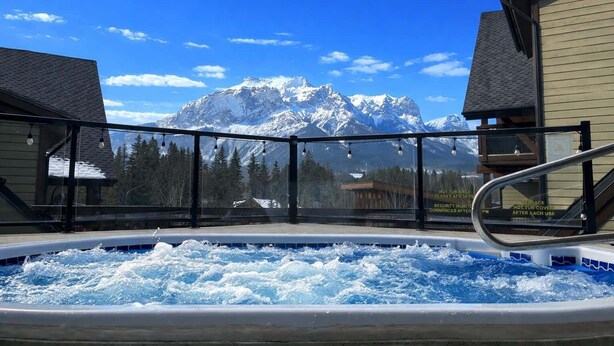 A hot tub with a mountain view, surrounded by buildings. - Creekside at Rundle Cliffs Lodge (Canmore)