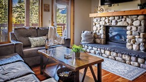 A cozy living room with a stone fireplace, leather sofas, and a wooden coffee table. - Creekside at Rundle Cliffs Lodge (Canmore)