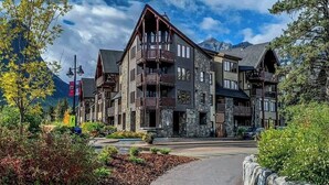 A multi-story lodge with a stone facade, balconies, and a mountain backdrop. - Creekside at Rundle Cliffs Lodge (Canmore)