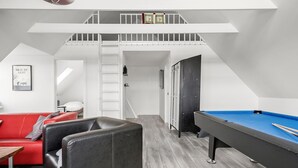 Un dormitorio estilo loft moderno con mesa de billar, un sofá rojo y una escalera que lleva a un nivel superior.