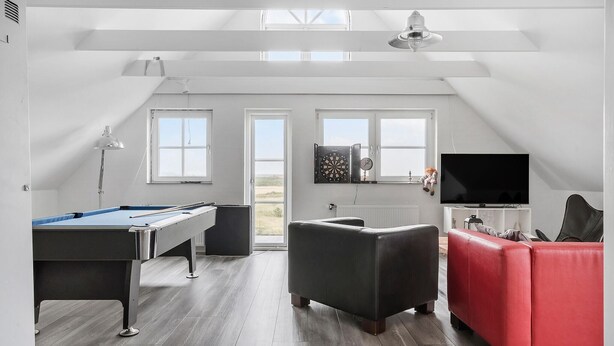 Una habitación amplia con mesa de billar, sofá rojo, televisión y dardos.