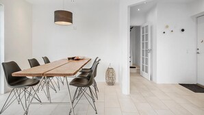 Un comedor moderno con una mesa de madera y sillas negras, una lámpara colgante y una puerta blanca con panel de vidrio.