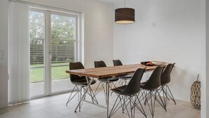 Un comedor con una mesa de madera y sillas negras, un lámpara colgante y vista a un jardín a través de una puerta corrediza de vidrio.