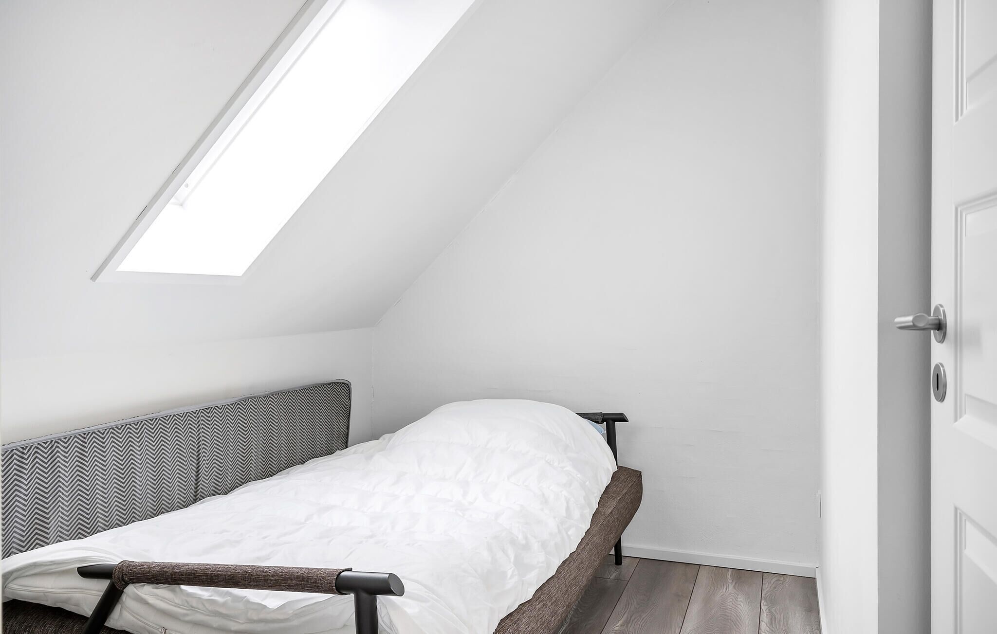 Ein kleines Zimmer mit einem Einzelbett, geneigter Decke und einem Oberlicht.