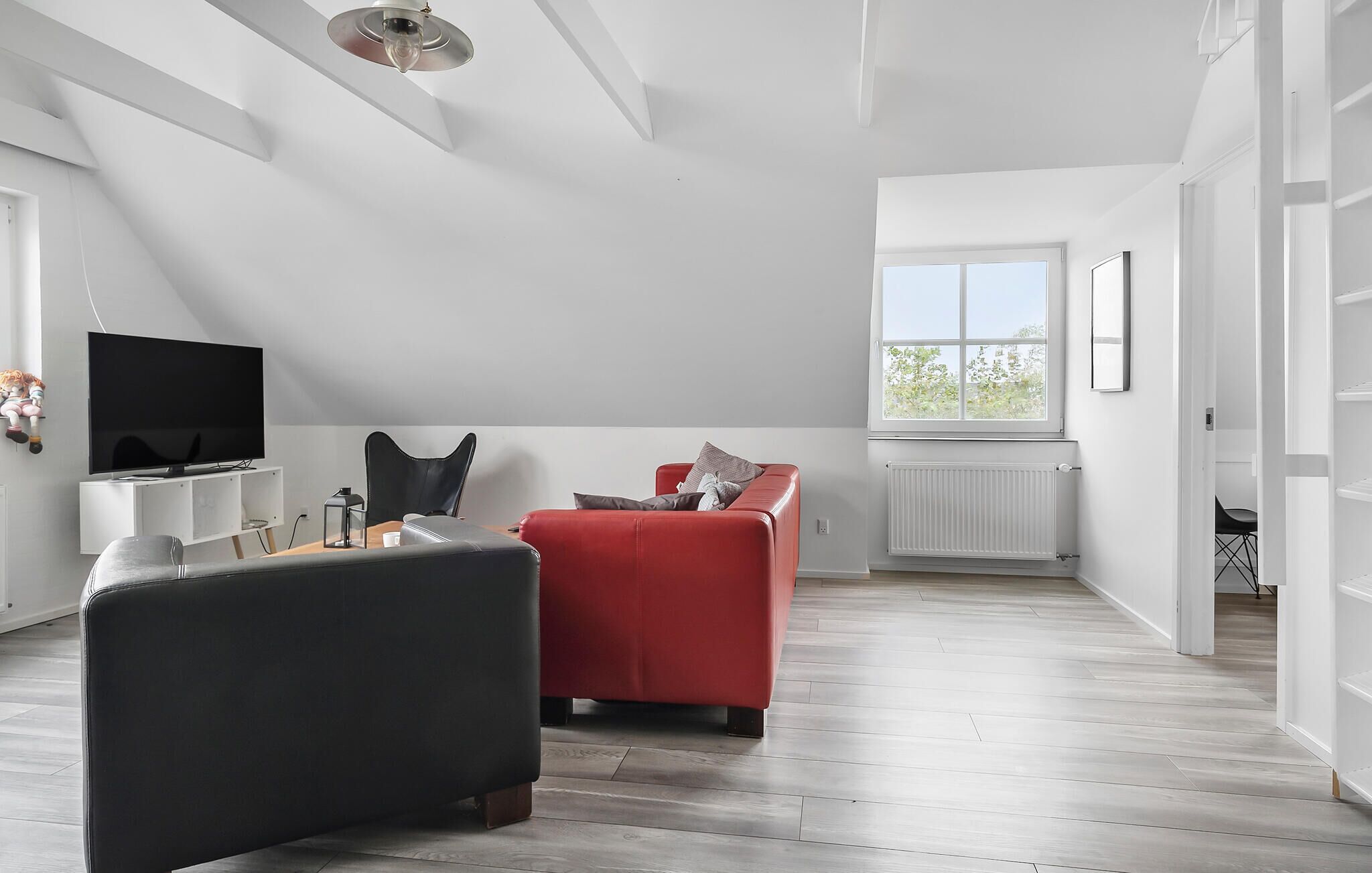 Un salon moderne avec un canapé rouge, un fauteuil noir et un téléviseur à écran plat posé sur une console blanche.
