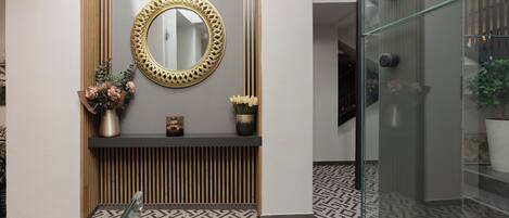 Un baño moderno con piso de patrón geométrico, un espejo redondo con marco decorativo, y una repisa con flores y una planta pequeña.