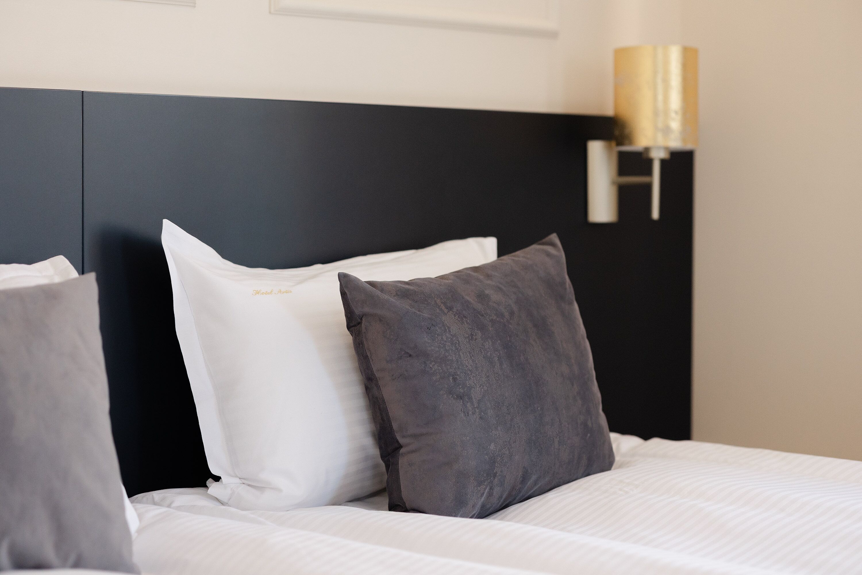 A neatly made bed with white and gray bedding, a black headboard, and a wall-mounted lamp.