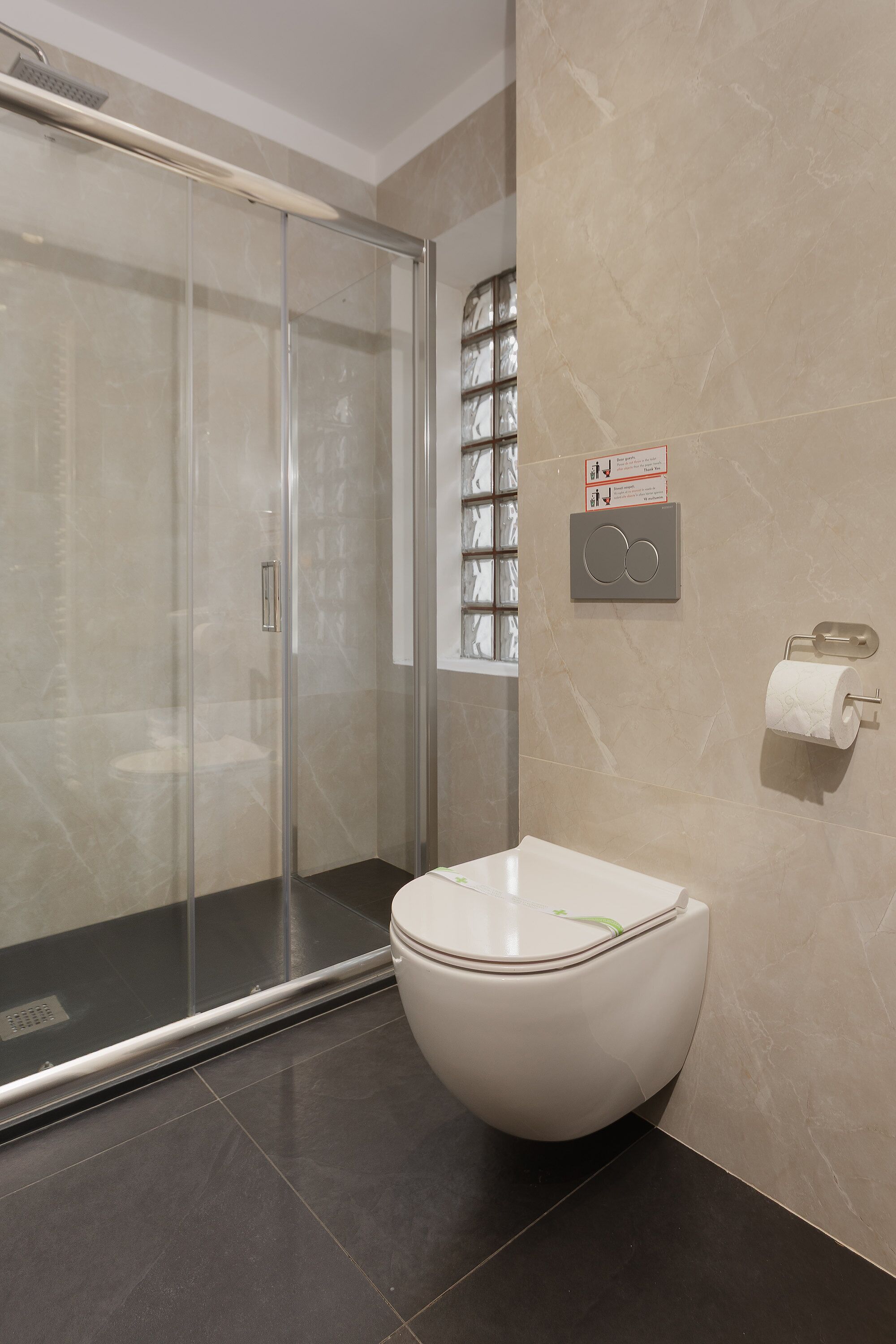 Une salle de bain moderne avec une douche à parois de verre, des toilettes blanches et un mur recouvert de carreaux de marbre.