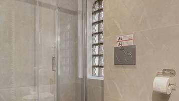 Une salle de bain moderne avec une douche à parois de verre, des toilettes blanches et un mur recouvert de carreaux de marbre.