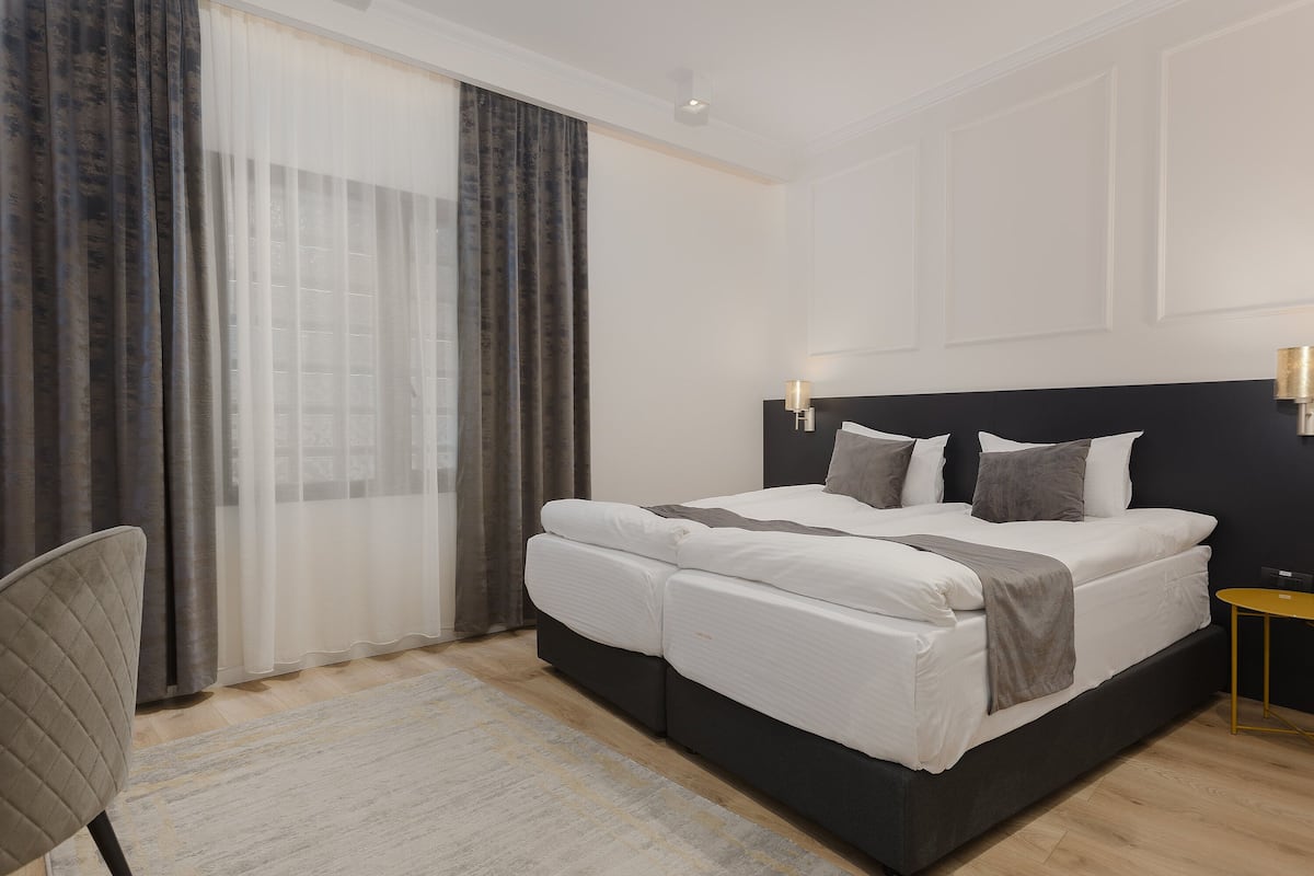 A modern hotel room with a large bed, a chair, a small table, and a large window with curtains.