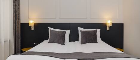 A neatly made bed with white linens and a gray throw blanket, two bedside lamps, and a small round table.
