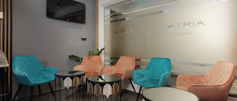 Eine moderne Hotelhalle mit Sitzgelegenheiten, einem Flachbildfernseher und einer Glaswand mit dem Hotelnamen.