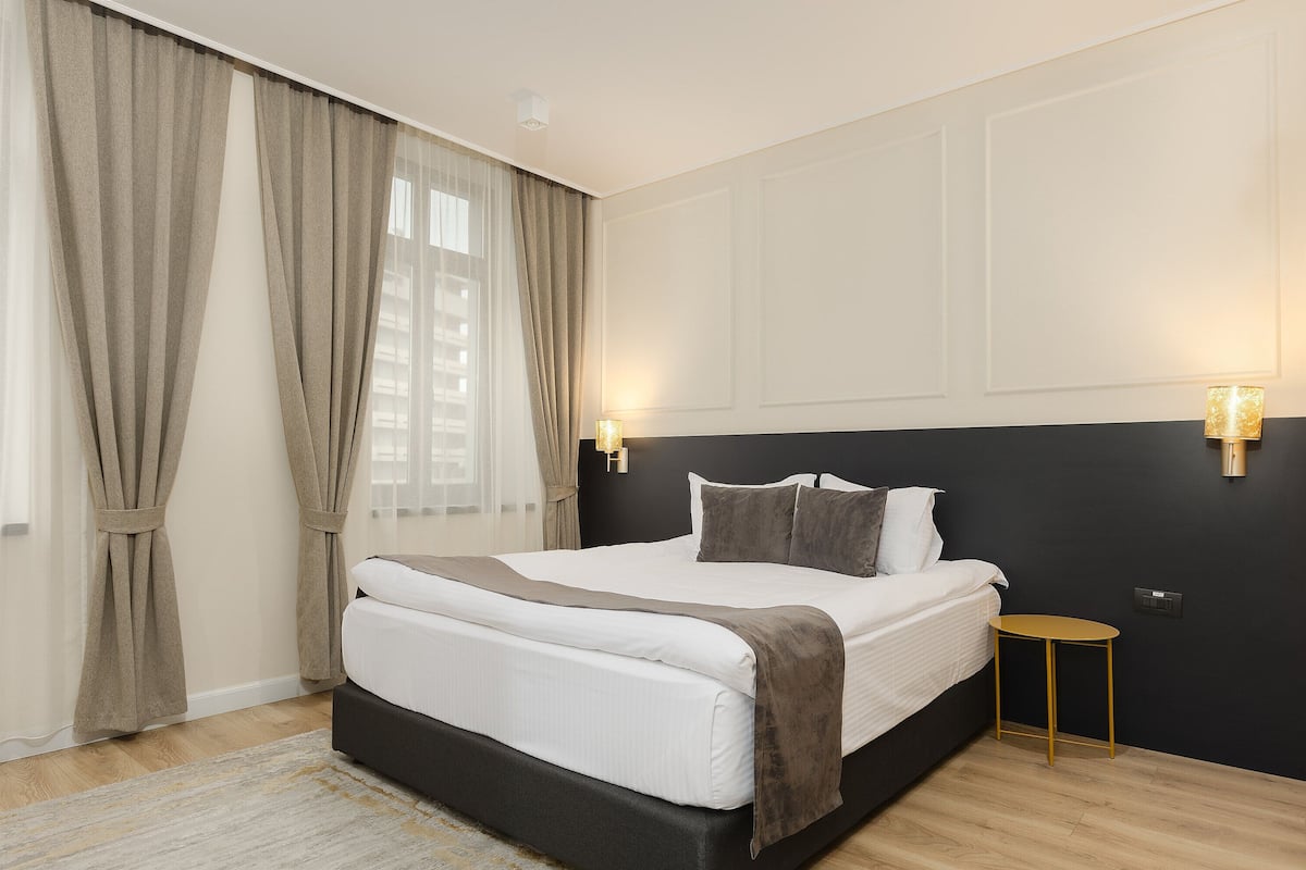 A bedroom with a bed, curtains, a bedside table, and wall-mounted lights.