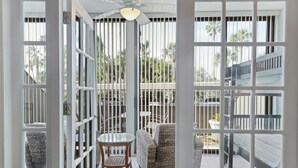 Un patio cubierto con mesa de vidrio y muebles de mimbre, delimitado por puertas de vidrio con marcos blancos y barras verticales.