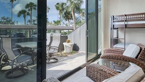 Un balcón moderno al aire libre con puerta de vidrio, mobiliario de mimbre y vistas a palmeras.