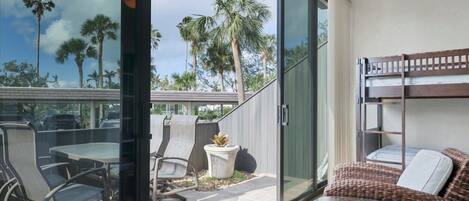 A modern outdoor balcony with a glass door, wicker furniture, and a view of palm trees.