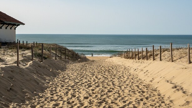 A sandy beach with a wooden fence and a building with a red roof.