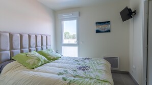 A bedroom with a bed, a window, a painting, and a TV mounted on the wall.
