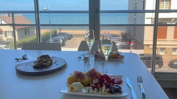 A table with a meal and glasses of white wine, overlooking a beach and ocean.