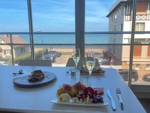 Een tafel met eten en glazen witte wijn, met uitzicht op een strand en oceaan.