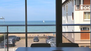 A view from a window overlooking a beach with parked cars and a sailboat in the distance.