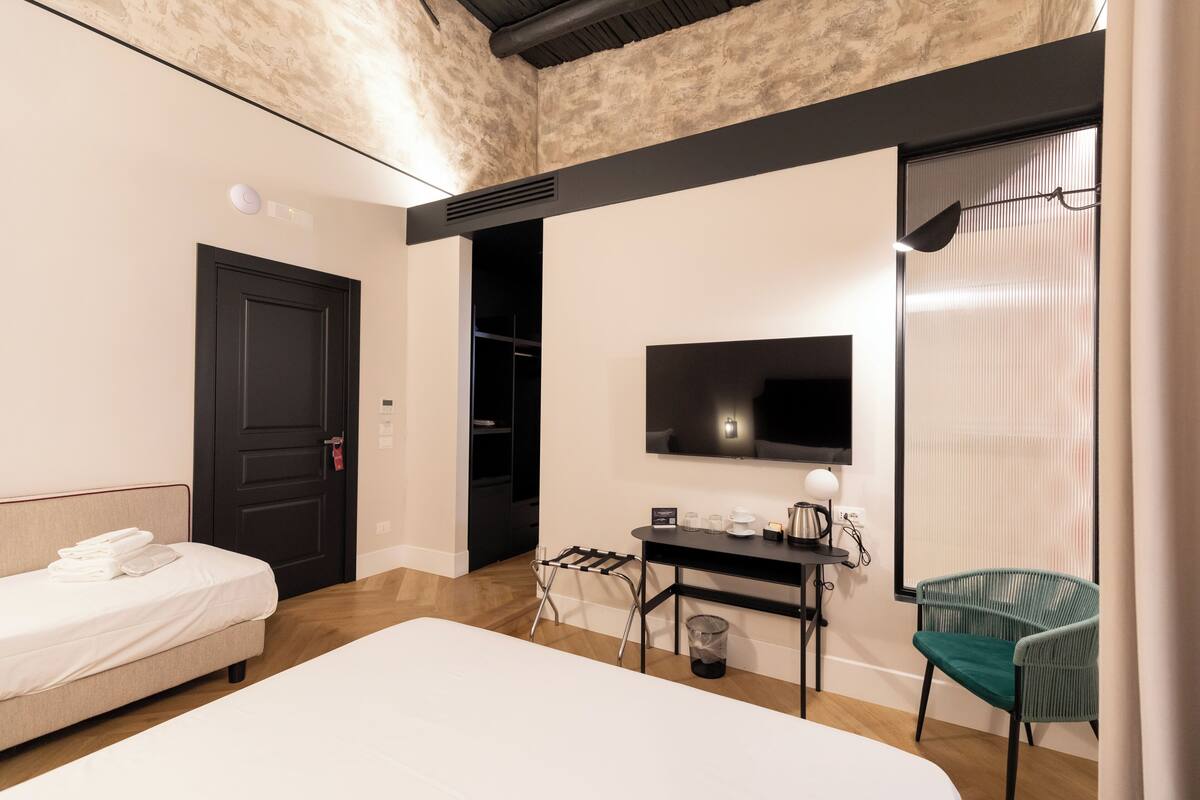 A modern hotel room with a bed, desk, chair, TV, and a wardrobe.