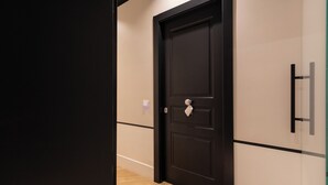 A hallway with a black door, a light switch, and a glass partition. - Relais Ammira (Naples)