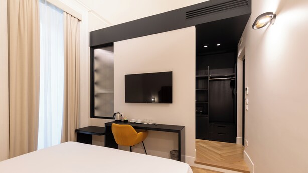 A hotel room with a bed, a desk, a chair, a TV, a wardrobe, and a bathroom visible through an open door. - Relais Ammira (Naples)