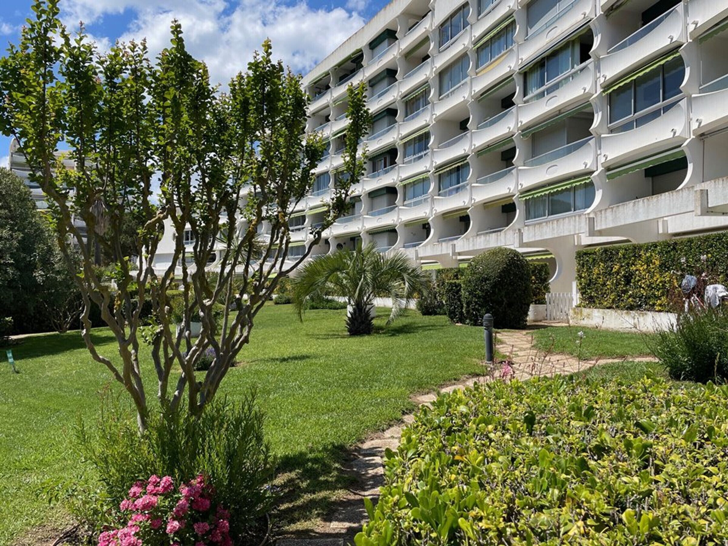A modern hotel with a multi-story structure, a well-maintained garden with various plants and flowers, and a clear sky.