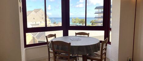 Habitación esquinera con ventanal panorámico que ofrece vistas al mar, una mesa redonda con sillas y una lámpara de pie.