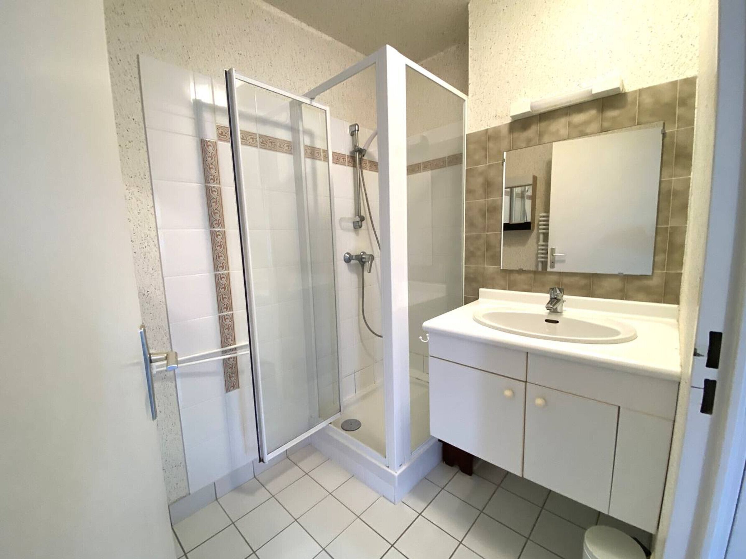 A modern bathroom with a glass-enclosed shower, a white sink, and a large mirror.