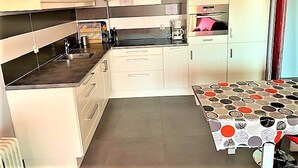 A compact kitchen with white cabinets, a black countertop, and a patterned tablecloth. - Stylish 1-Bed Apt in La Grande-Motte: Modern, Spacious, Loggia, Parking, Near Beach & Shops (La Grande-Motte)