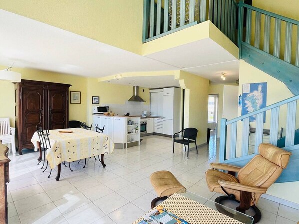 A spacious living area with a dining table, chairs, a sofa, and a staircase.
