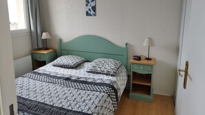 A bedroom with a bed, two bedside tables, a nightstand, a wall clock, and a window with curtains.