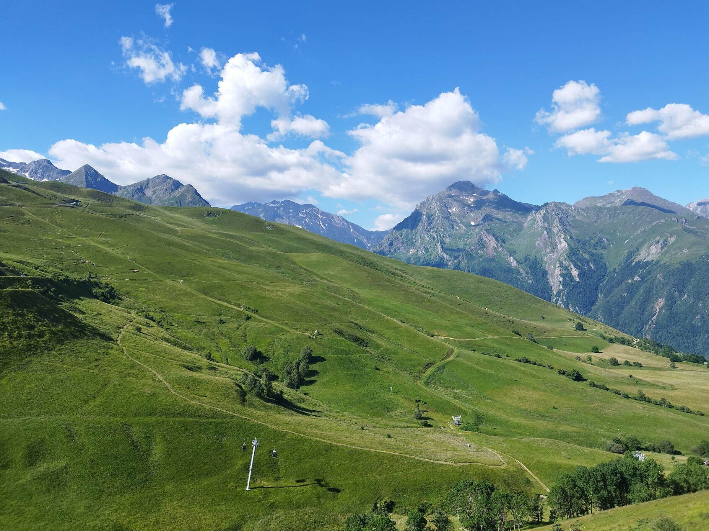 Uma vista panorâmica de uma paisagem montanhosa, com vales verdejantes e picos distantes sob um céu claro.