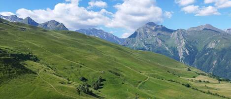 Uma vista panorâmica de uma paisagem montanhosa, com vales verdejantes e picos distantes sob um céu claro.