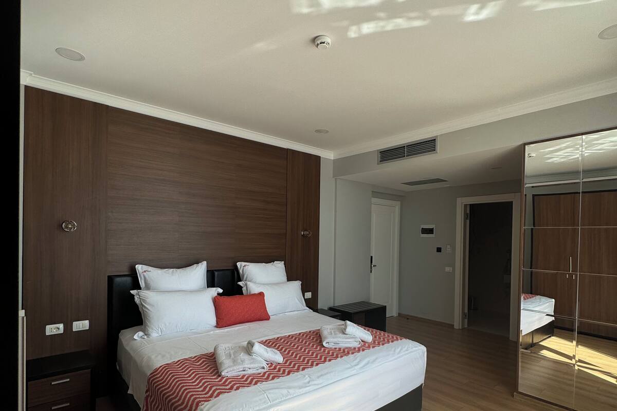 Quarto moderno com cama grande, painéis de madeira nas paredes, armário embutido e um espelho grande.