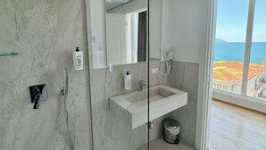 A modern bathroom with a glass shower enclosure, a large mirror, and a view of the sea through a large window. - Hotel Britania  (Vlorë)